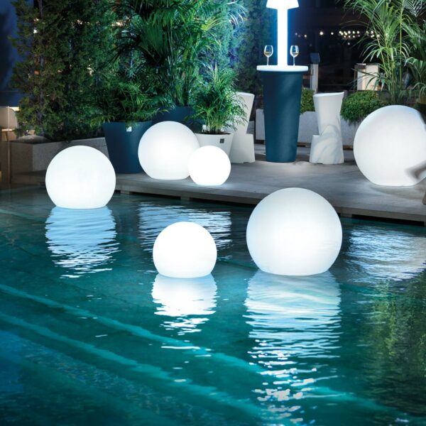 Vue nocturne d’un jardin avec plusieurs sphères lumineuses LED flottantes sur une piscine, créant une ambiance magique et élégante.